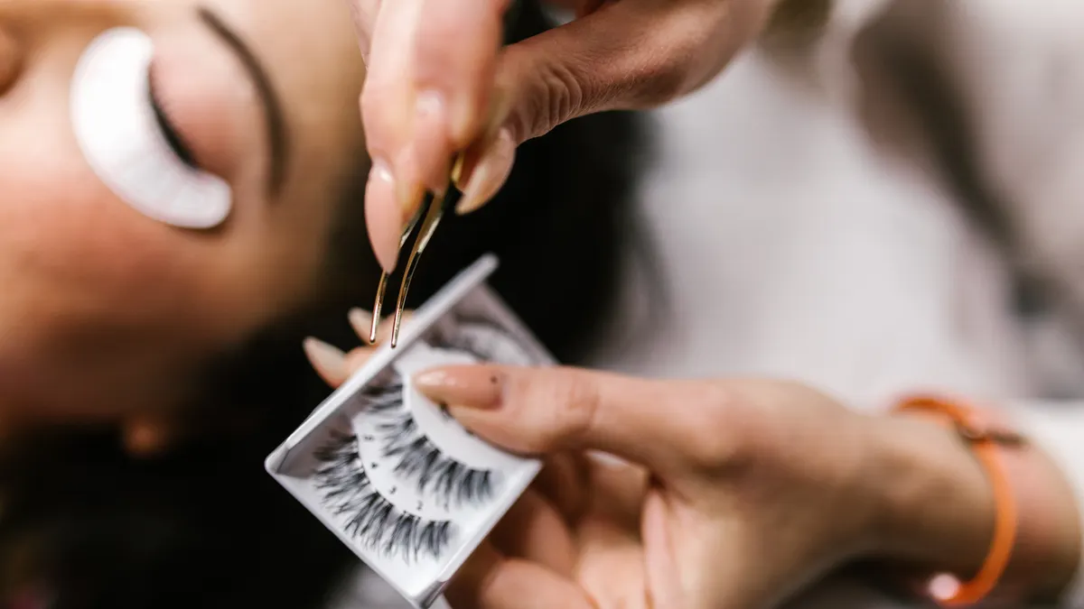 hands holding a false lash strip with tweezers
