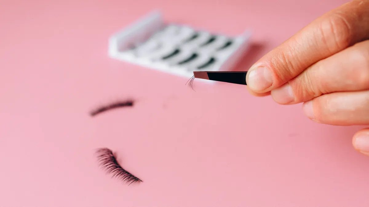 false eyelash strip and tweezers on pink background
